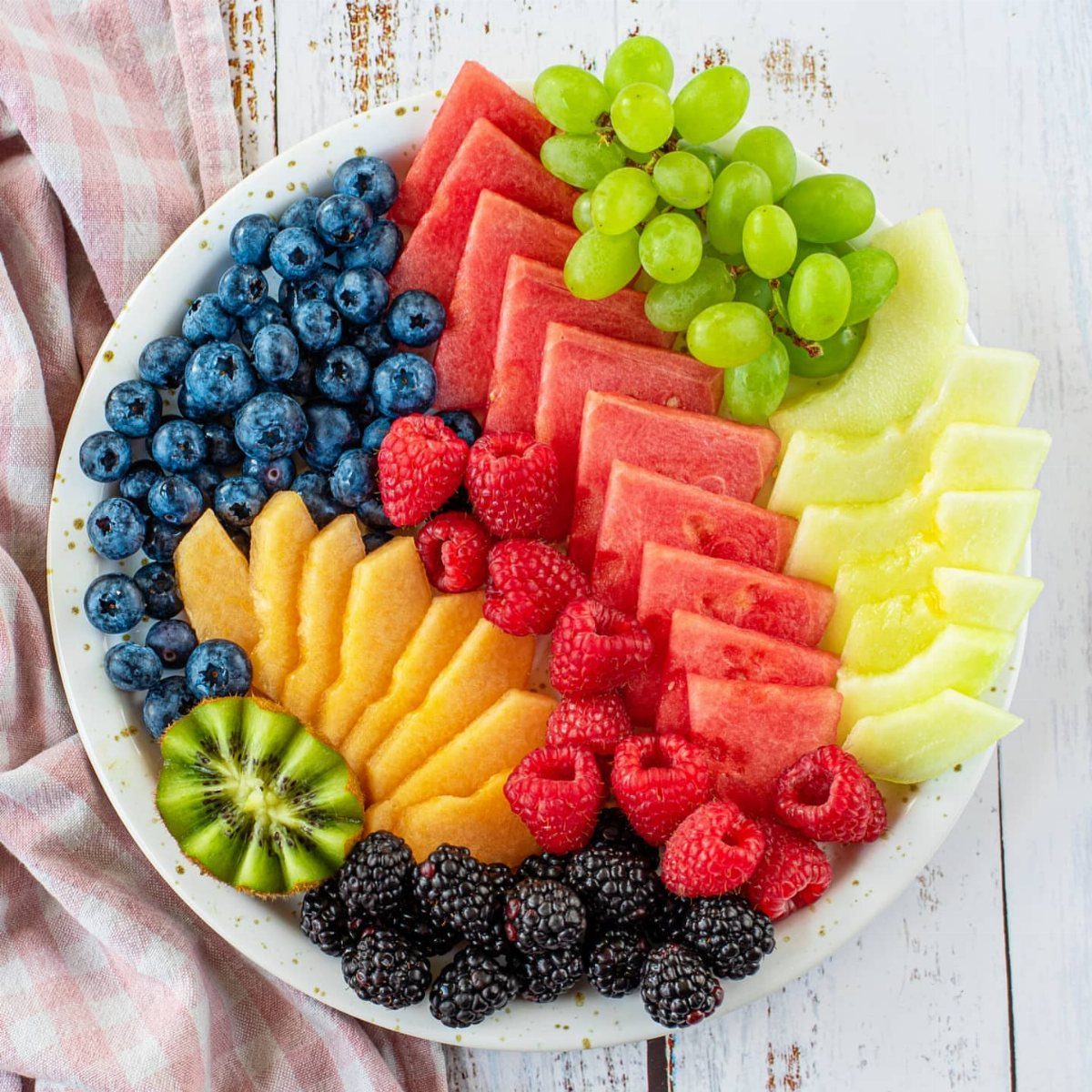 Fruit bowl filled with colorful arranged berries, melon, grapes, and kiwi slices.