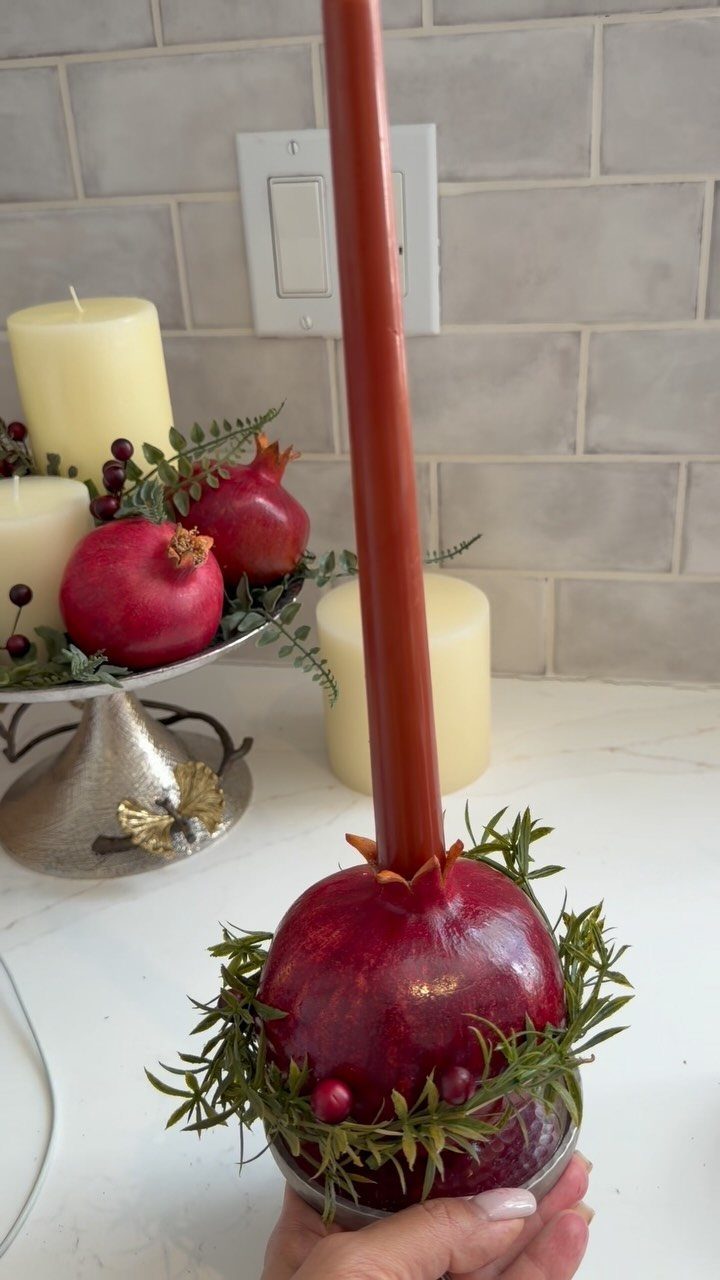 Red pomegranate candle holder with a taper candle and festive greenery decorations.