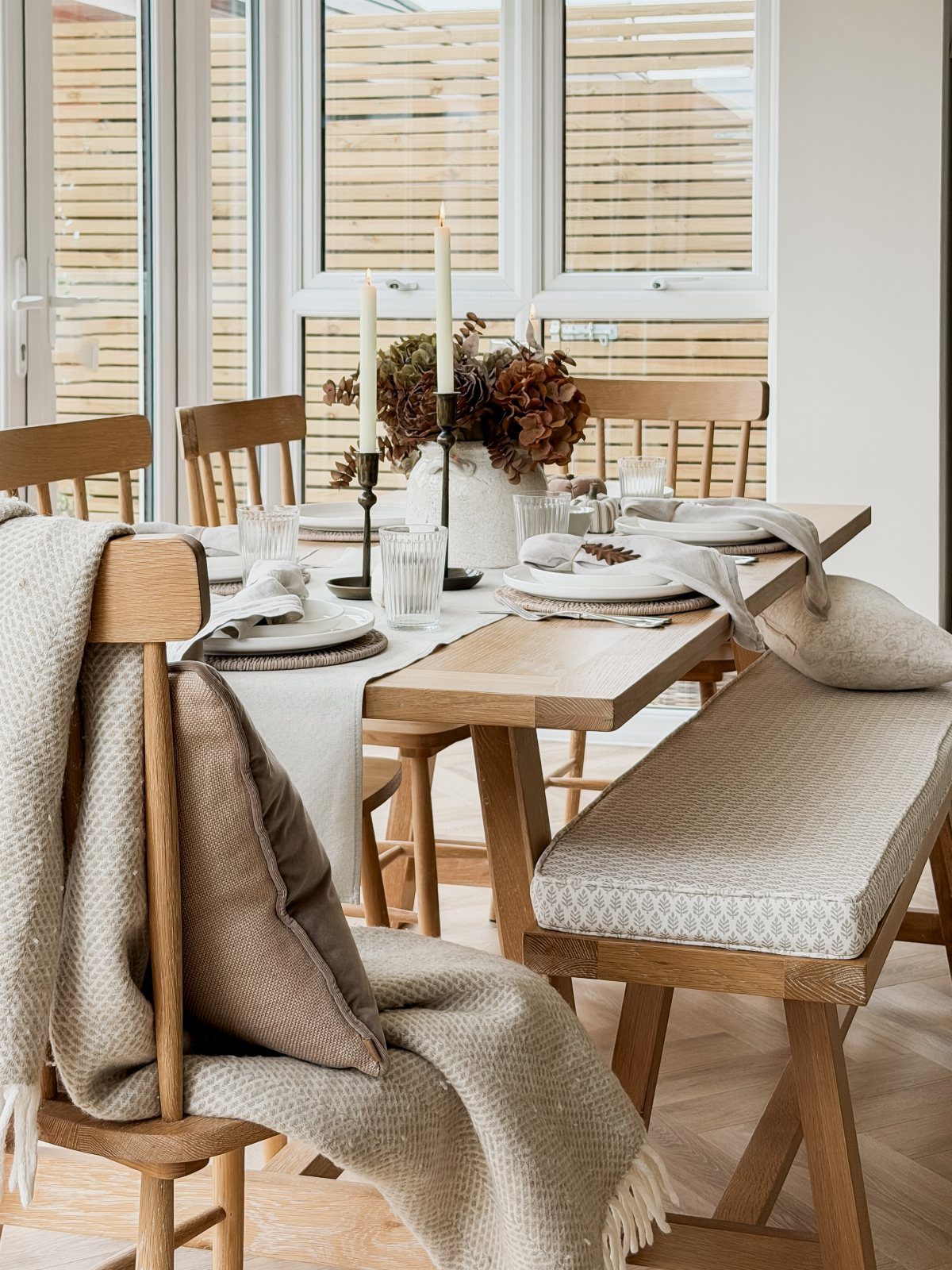 Beige fabric table runner on a wooden dining table with candles and foliage.