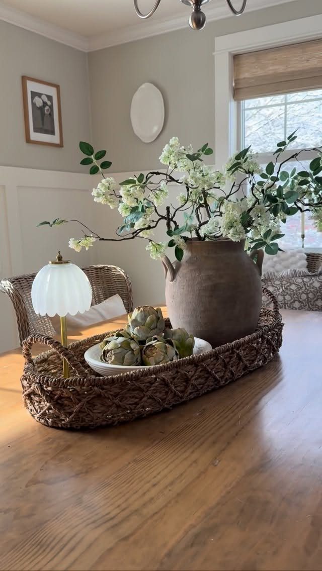 Woven tray centerpiece with white flowering branches in a clay vase and artichokes.