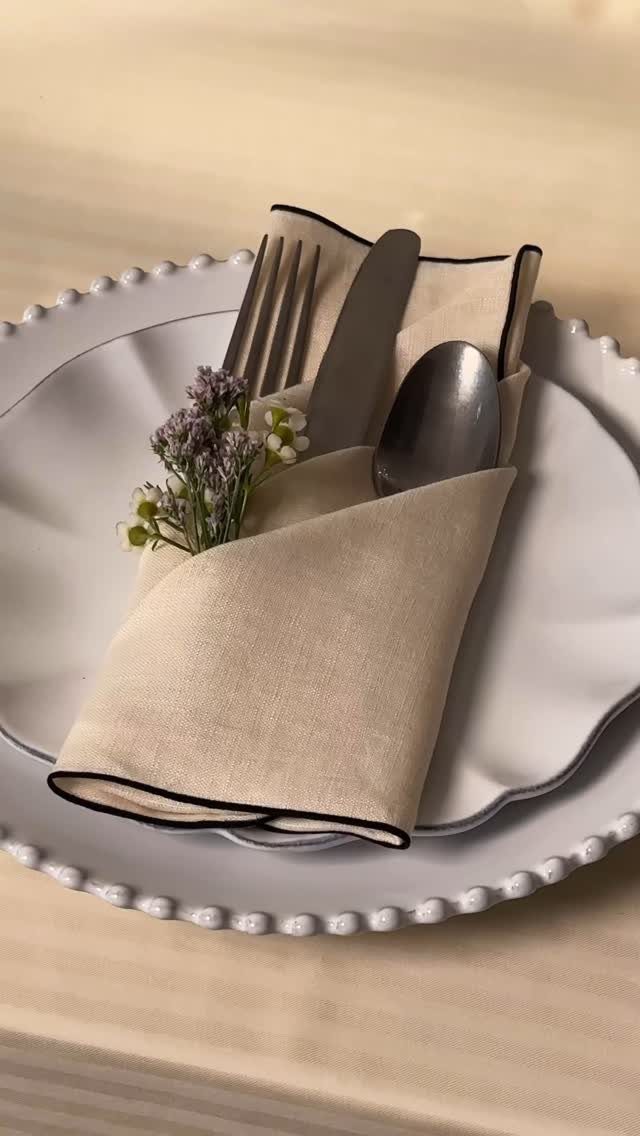 White beaded plate with a beige linen napkin, silver cutlery, and purple flowers.