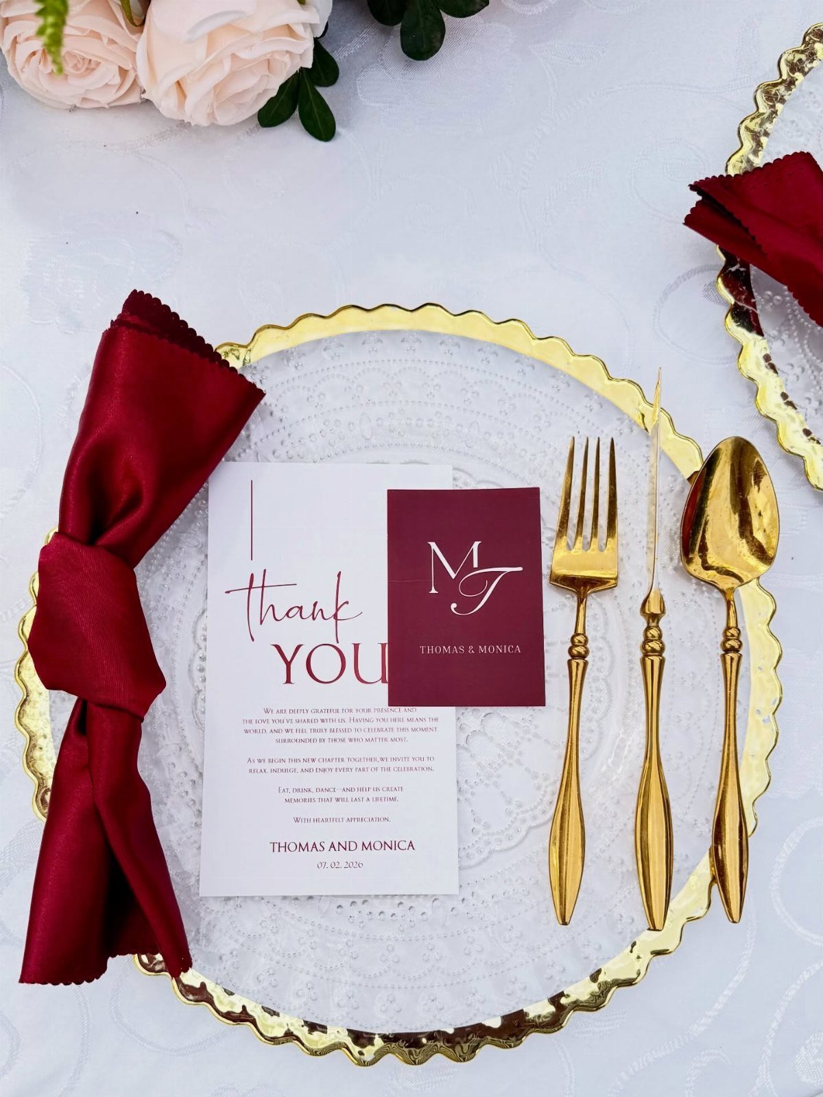 Gold-rimmed glass plate with gold cutlery, burgundy napkin, and thank you card.