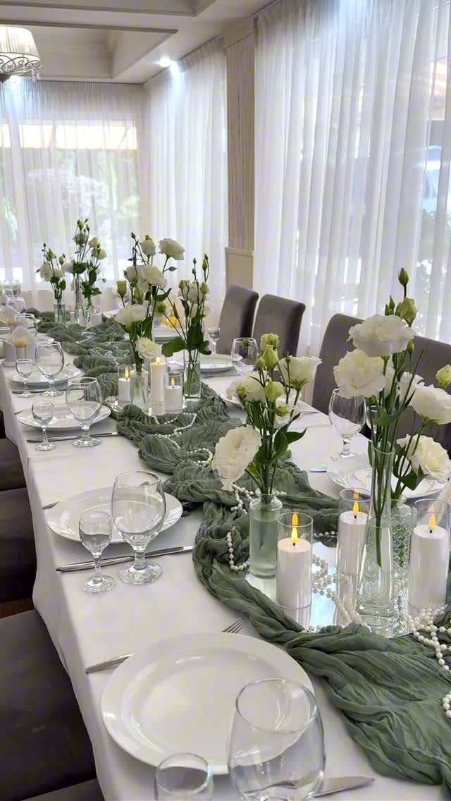 Formal table setting with white plates, glassware, white roses, and sage green runner.