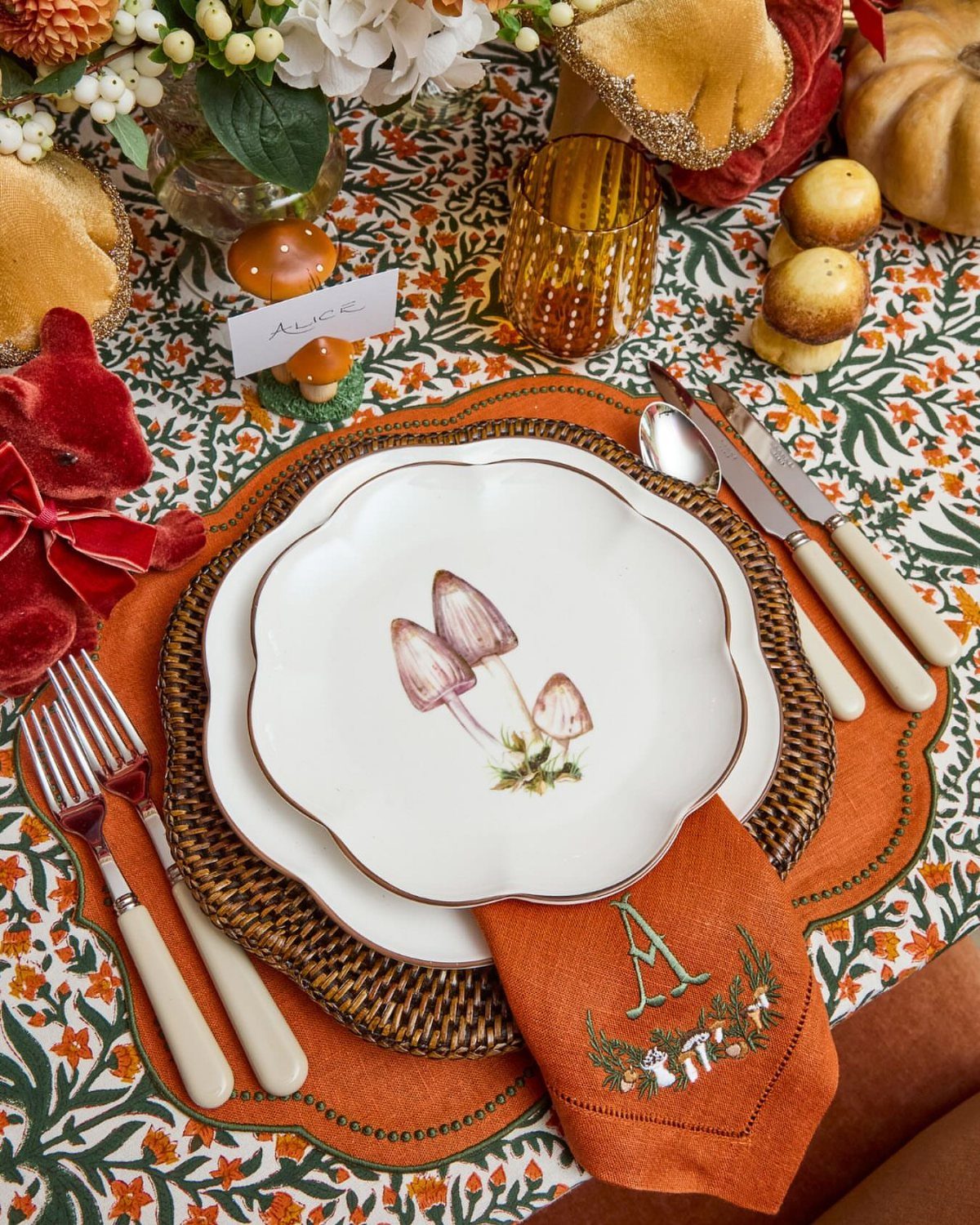Autumn table setting with mushroom plates, orange napkin, and floral tablecloth decorations.