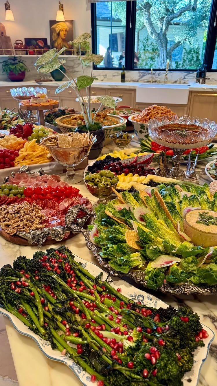 Buffet table with diverse platters of fresh vegetables, fruits, and charcuterie on marble.
