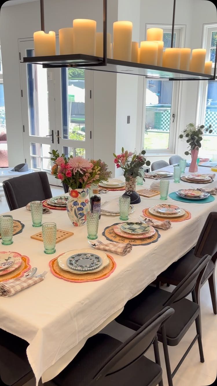 Dining table set with white cloth, colorful plates, green glasses, and floral arrangements.