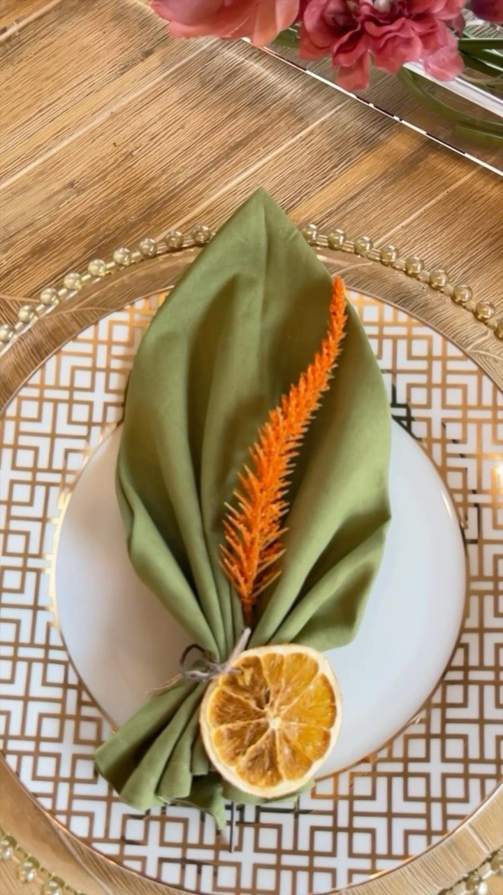 Place setting with olive green napkin, dried orange slice, and gold charger plate.