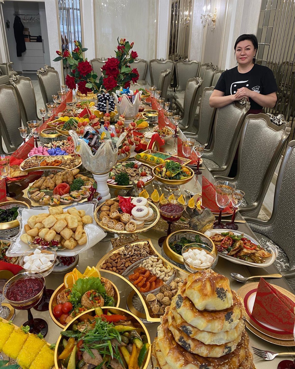 Long dining table filled with various food platters, red roses, and red napkins.