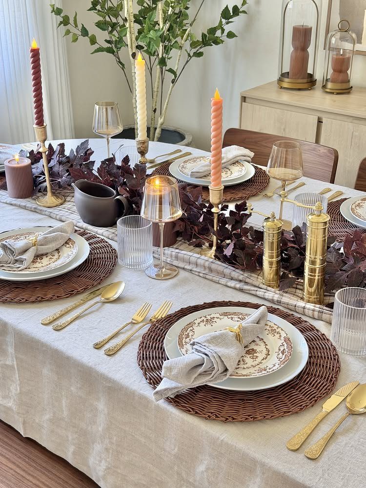 Dinner table with beige linens, striped runner, woven charger plates, and gold cutlery.