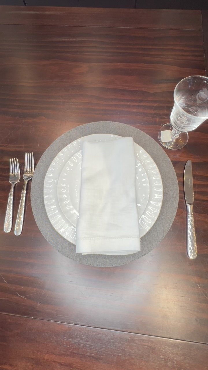 Table setting with white plates, silver cutlery, and a water glass on wood.