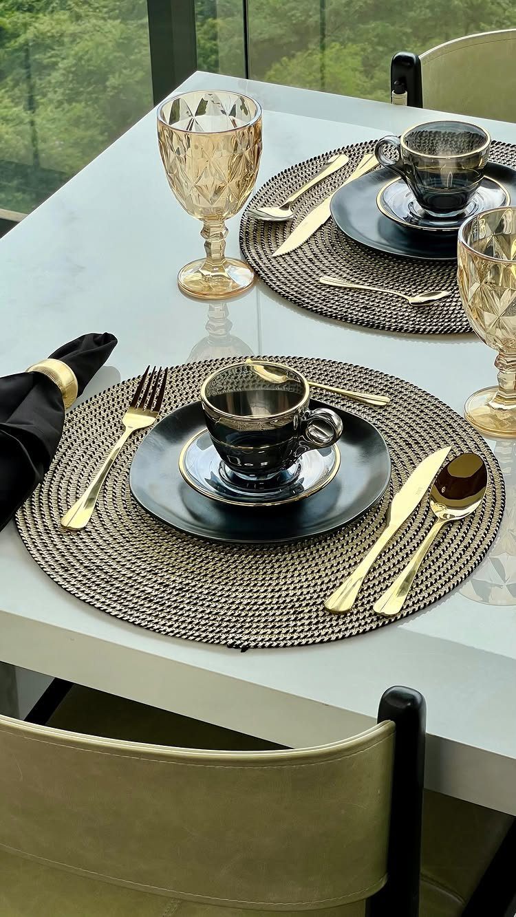 Table set with black plates, gold cutlery, and amber glasses on woven placemats.