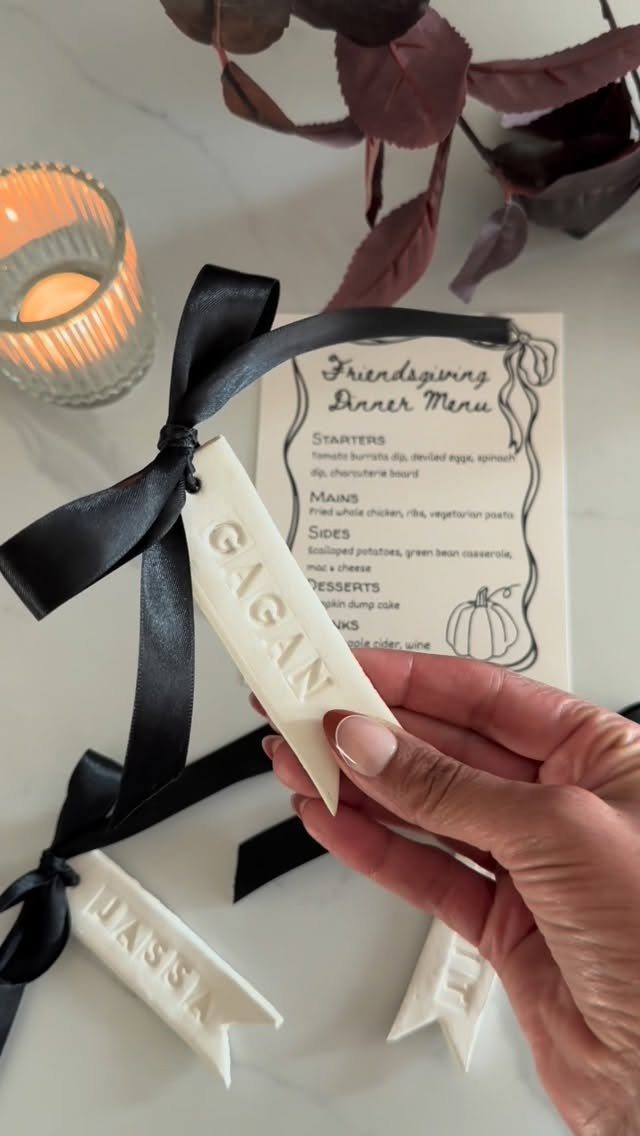 Hand holding a white name card next to a Friendsgiving dinner menu and candle.