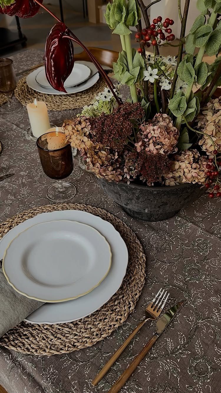 Table setting with woven placemats, white plates, and a large floral centerpiece.