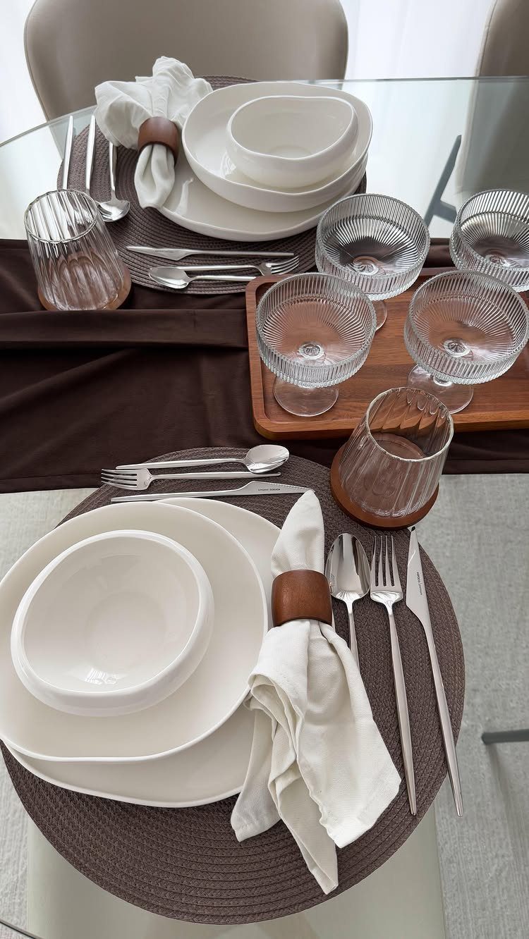 White ceramic dinnerware and ribbed glassware arranged on a brown dining table setup.