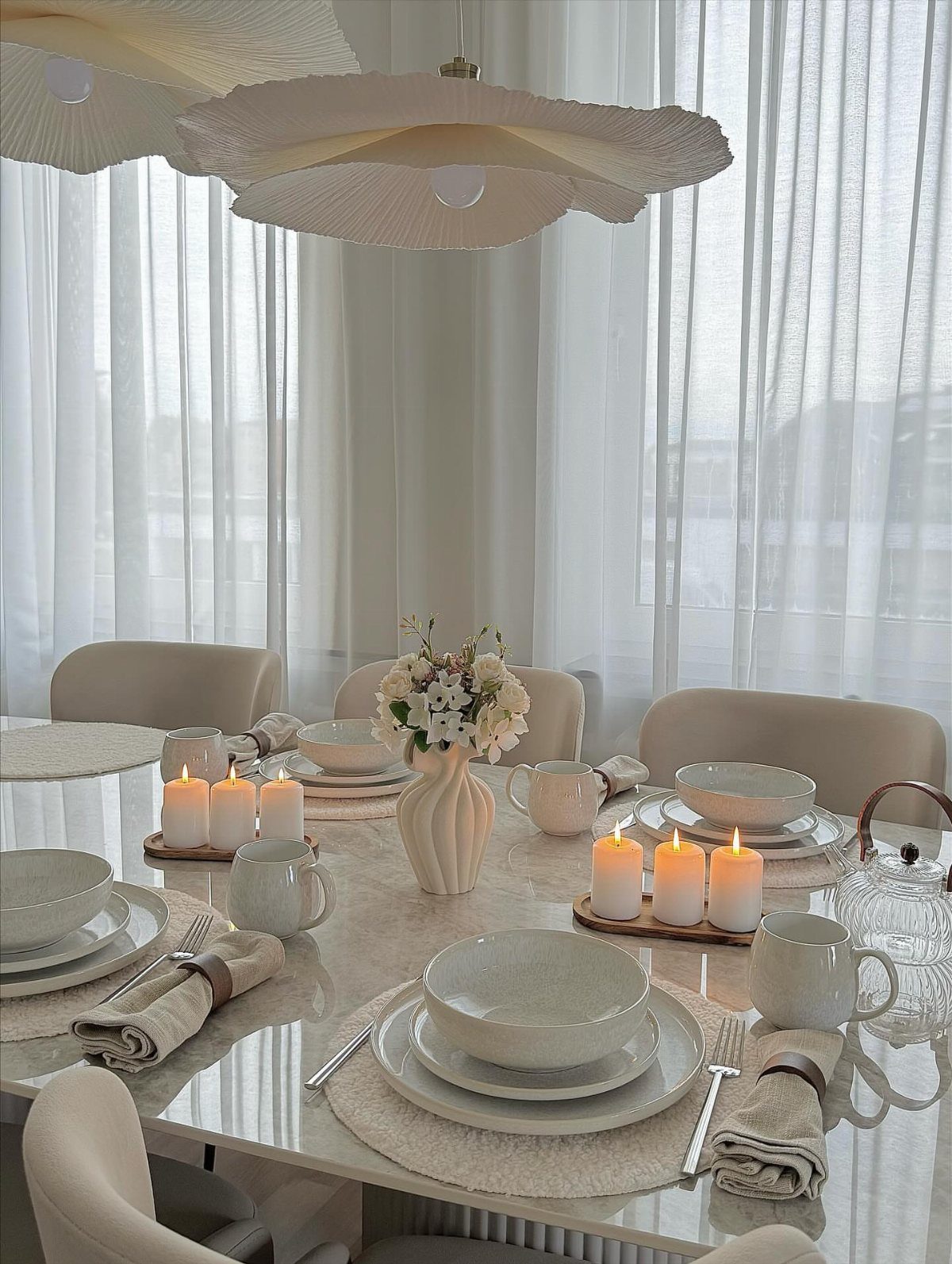 Neutral dinnerware set on a white table with candles and cream flowers.