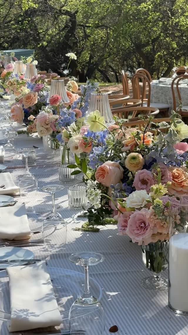 Outdoor dinner table with pastel pink and blue floral centerpieces and white linens.