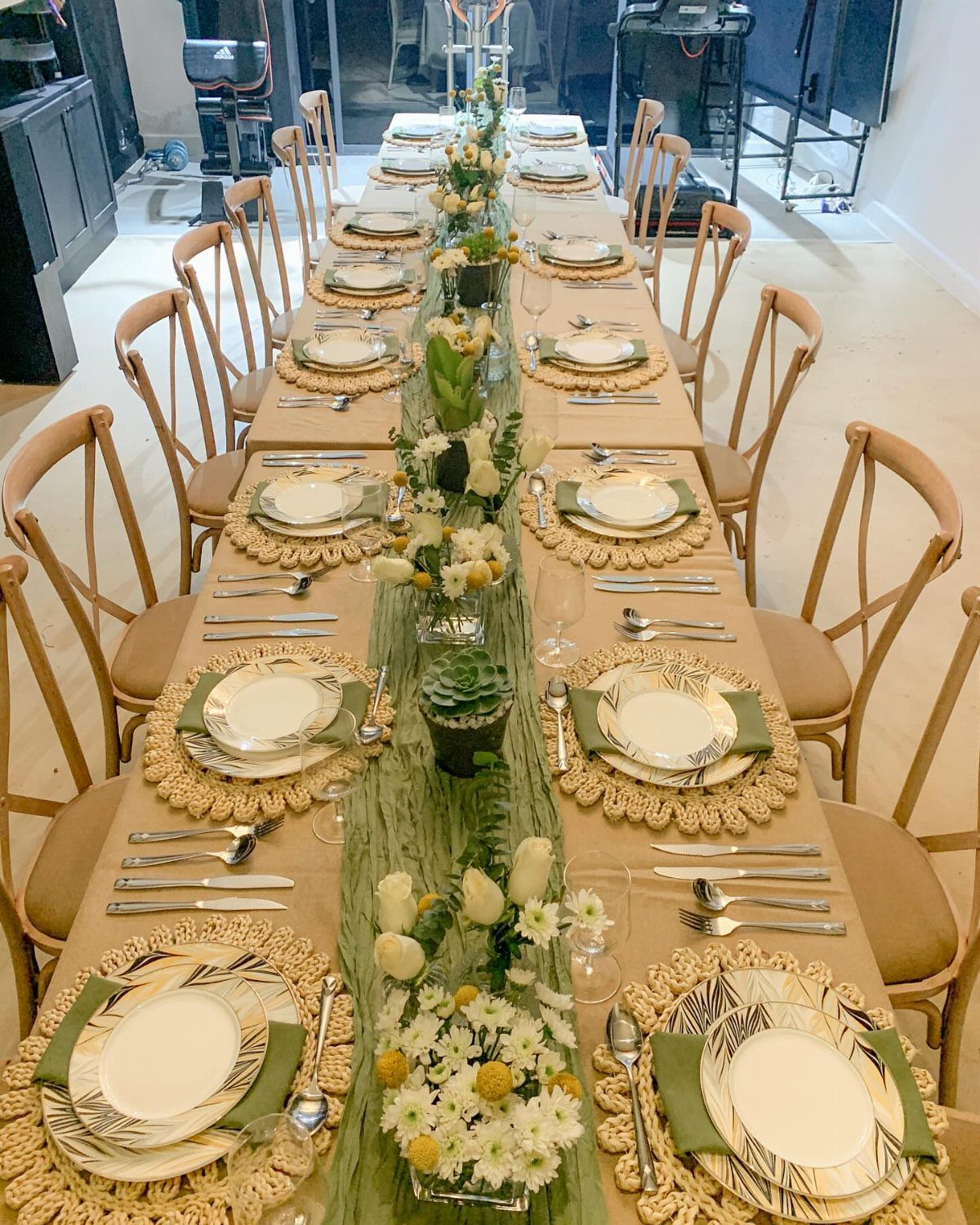 Long dinner table with woven placemats, green runner, and white floral centerpieces.