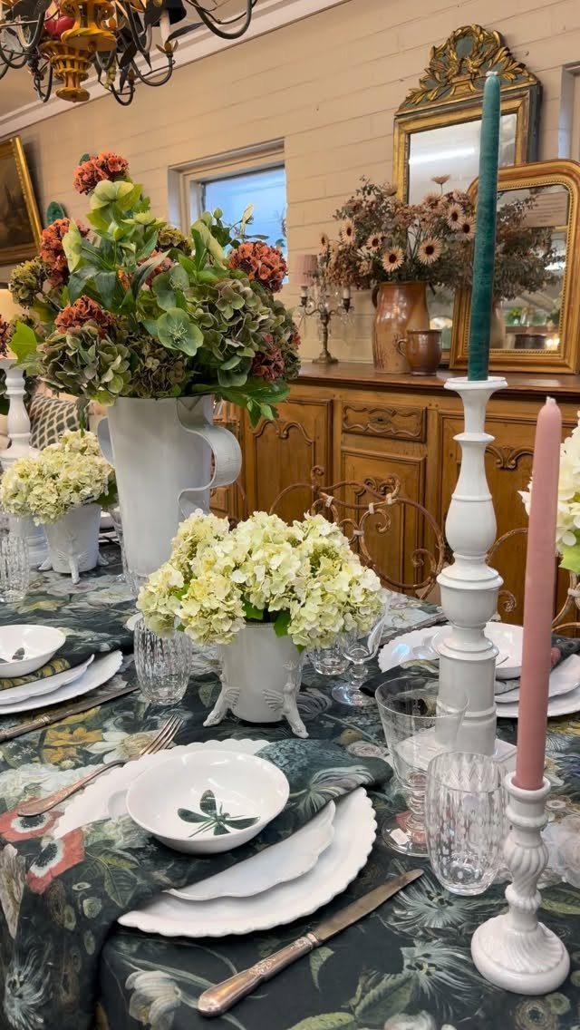 Dinner table setting with white plates, floral arrangements, and colorful tapered candles.