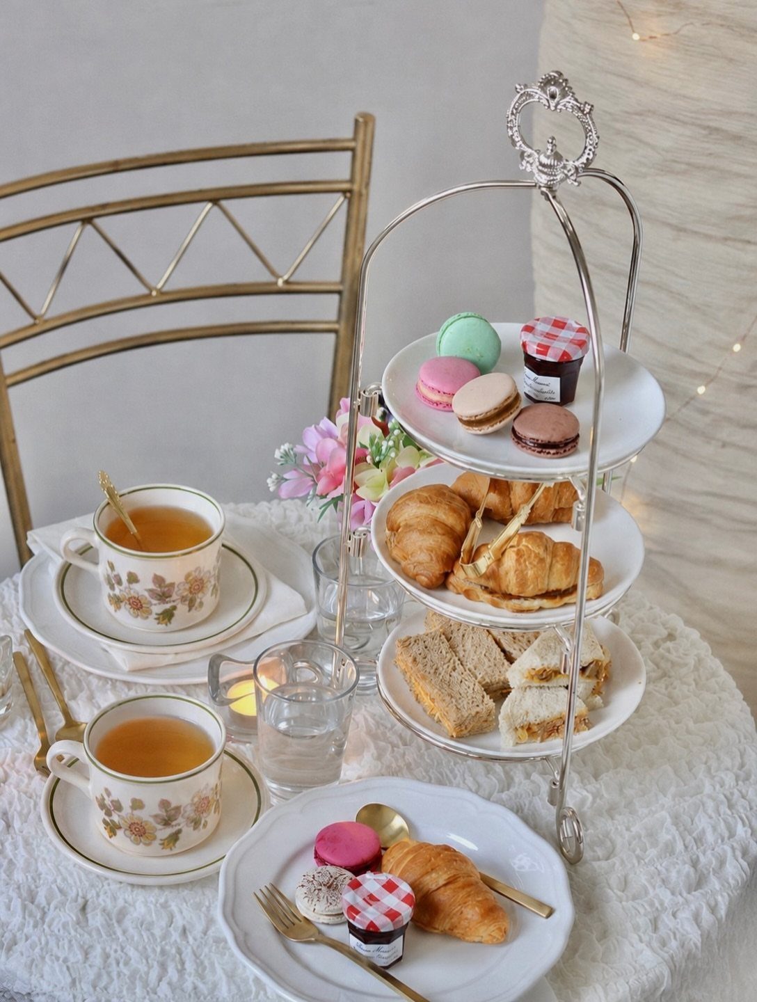 Three-tiered stand with tea treats and floral teacups on a white lace tablecloth