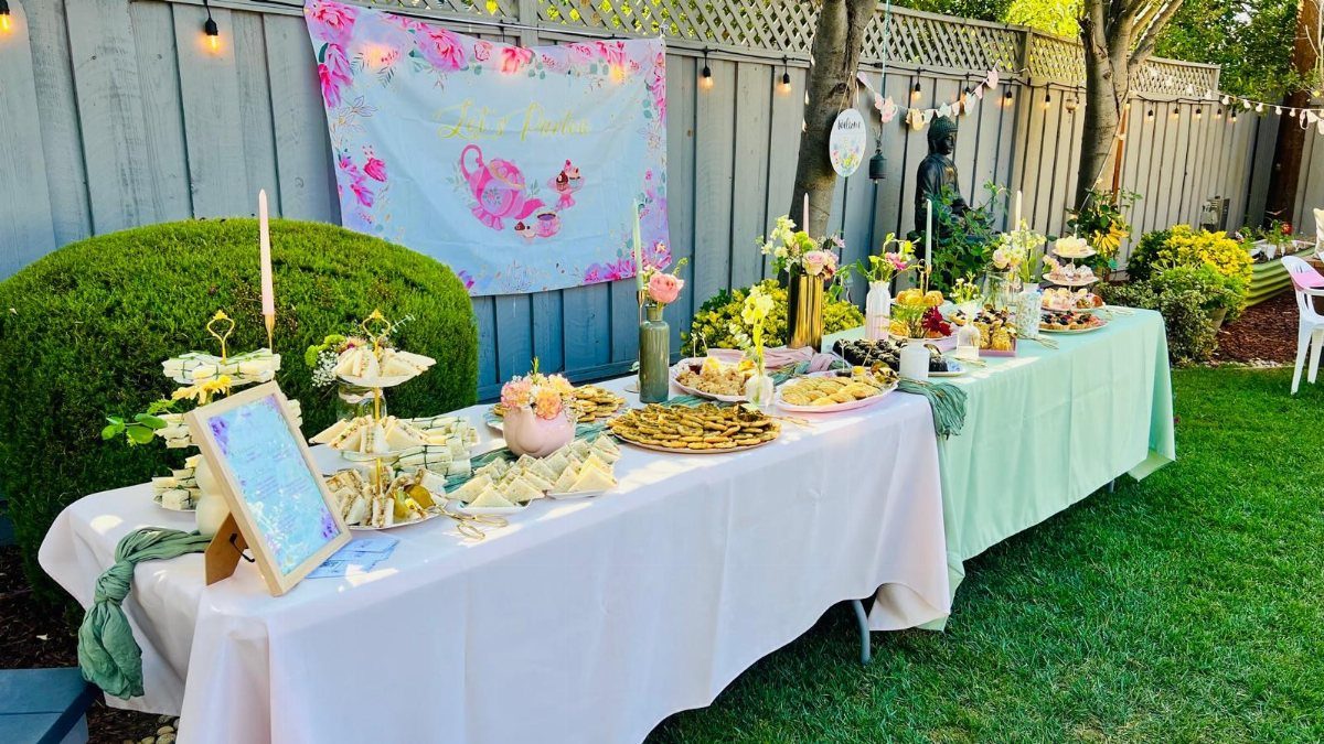 Outdoor tea party tables with white and mint linens, pastries, and floral decorations.