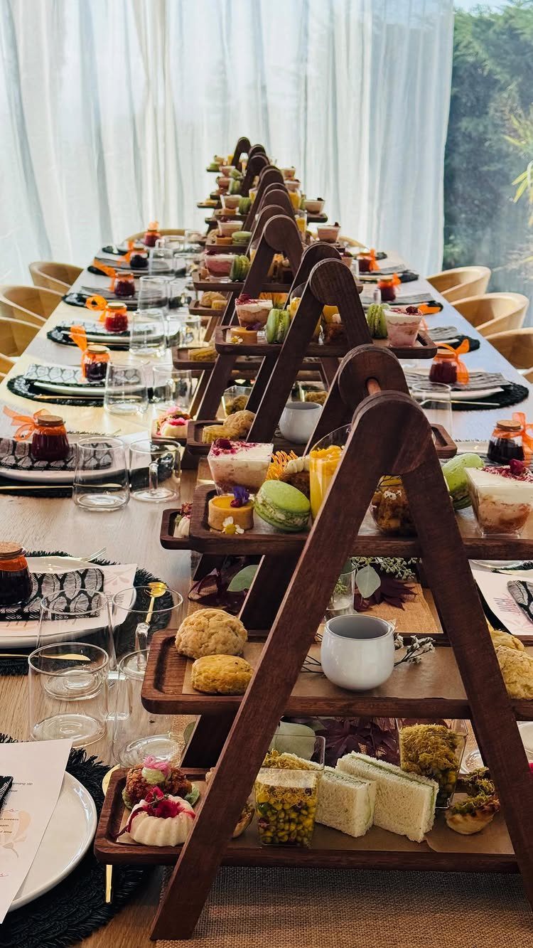 Formal tea party table with wooden tiered stands holding sandwiches and pastries.