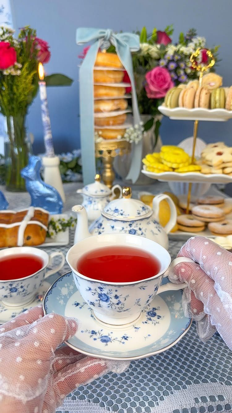 Floral porcelain teacups and a tiered dessert stand on a lace tea table.