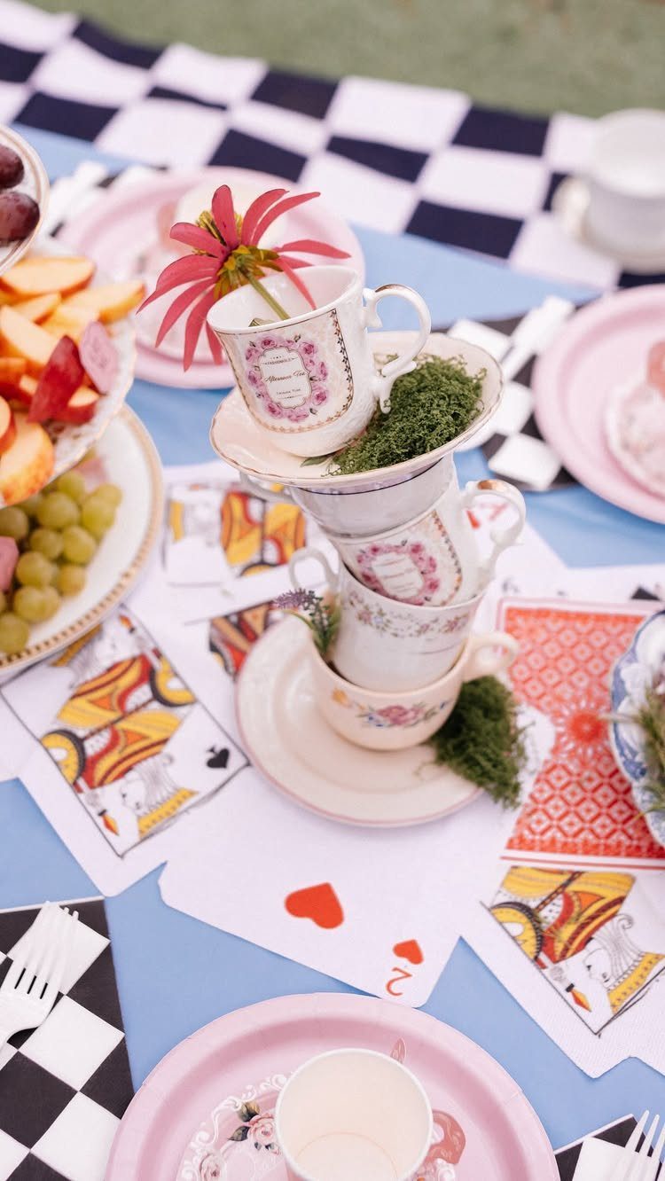 Stacked floral teacups and playing cards on a whimsical tea party table setup