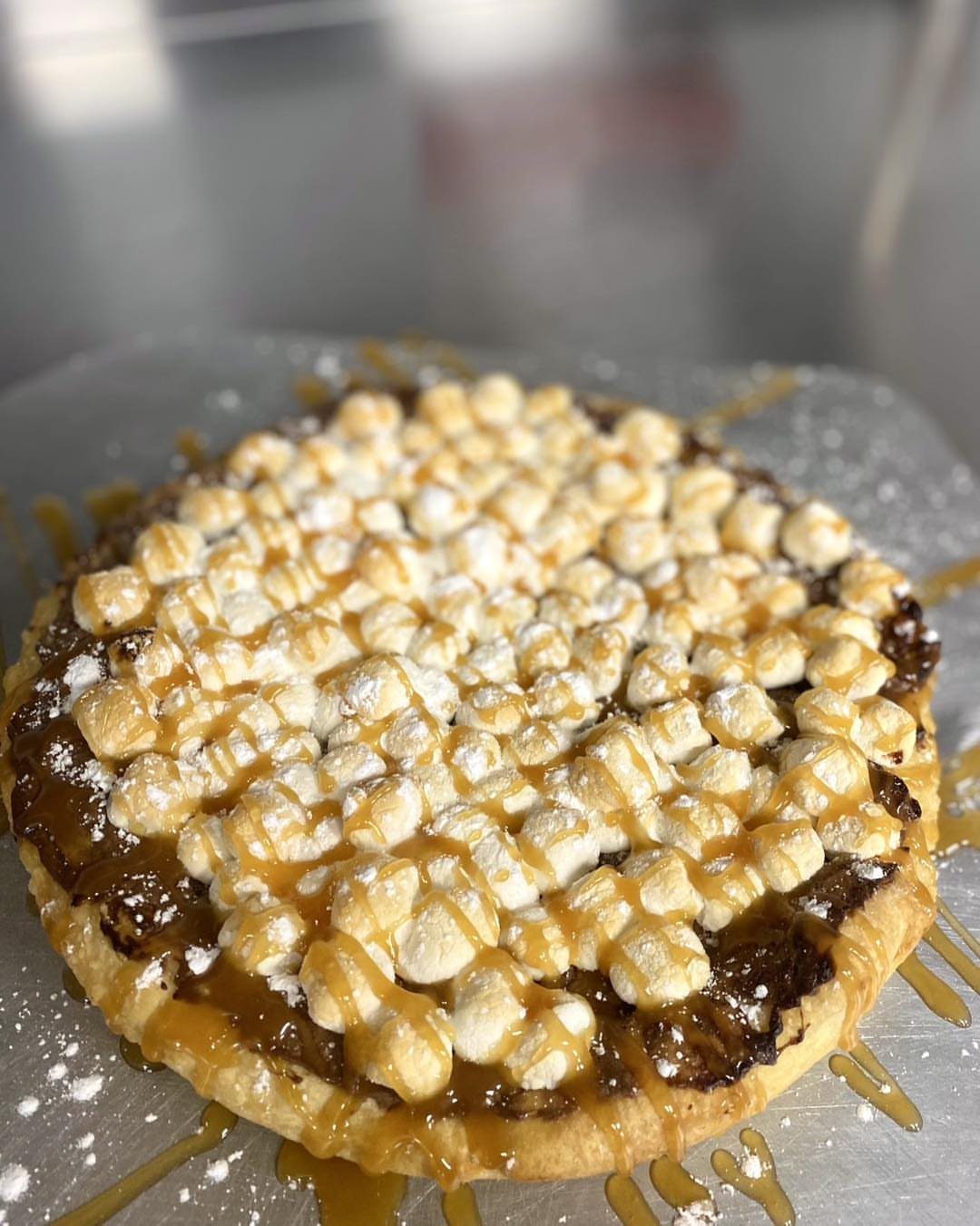 S'mores pie with toasted marshmallows, chocolate spread, and caramel drizzle on a tray.