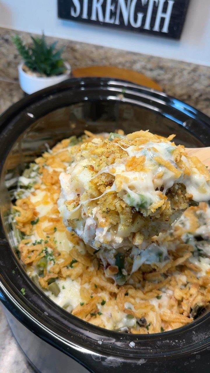 Cheesy potato casserole with crispy fried onions in a black slow cooker pot.
