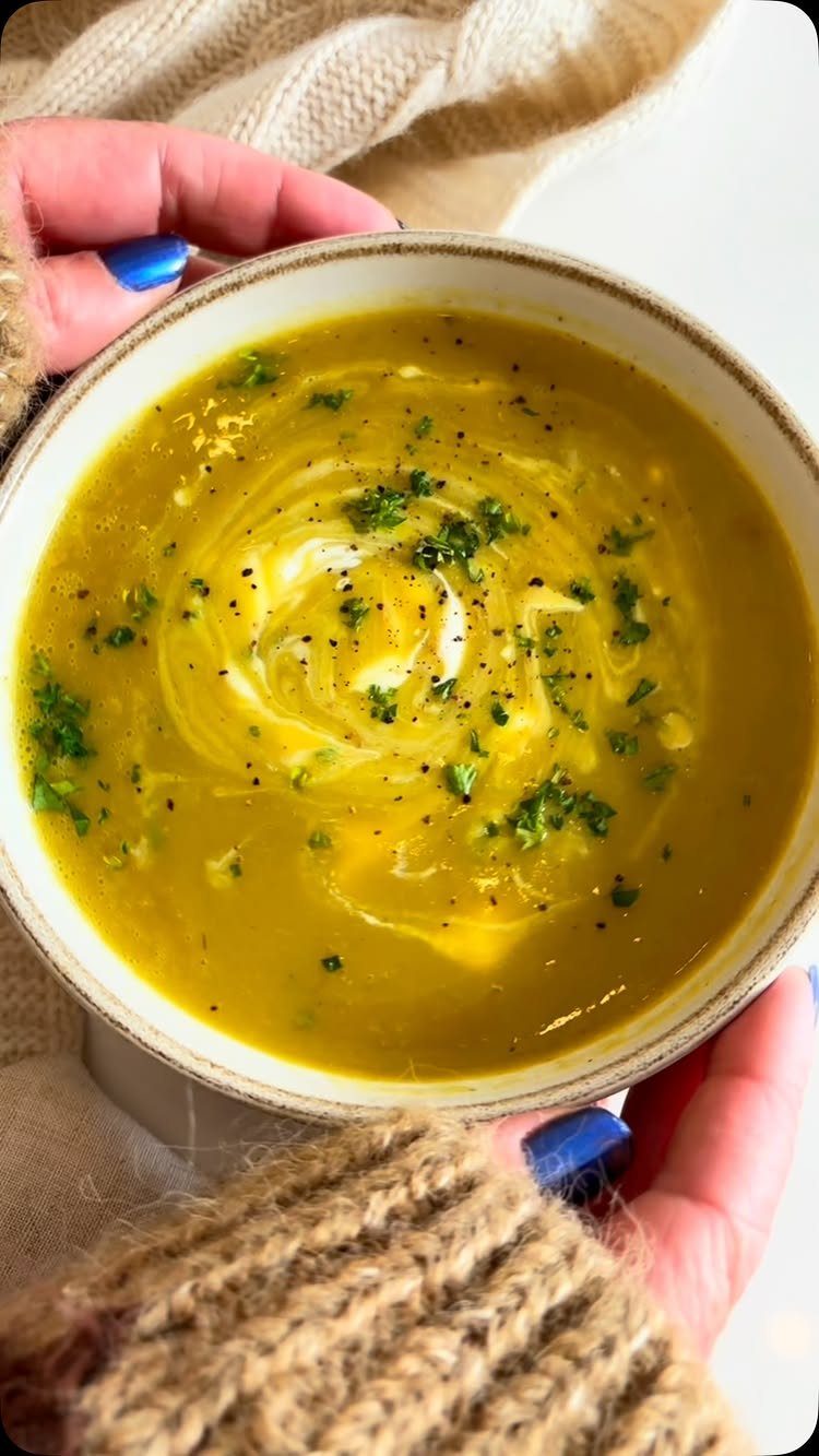 Creamy yellow-green potato leek soup with cream swirl and parsley in a bowl.