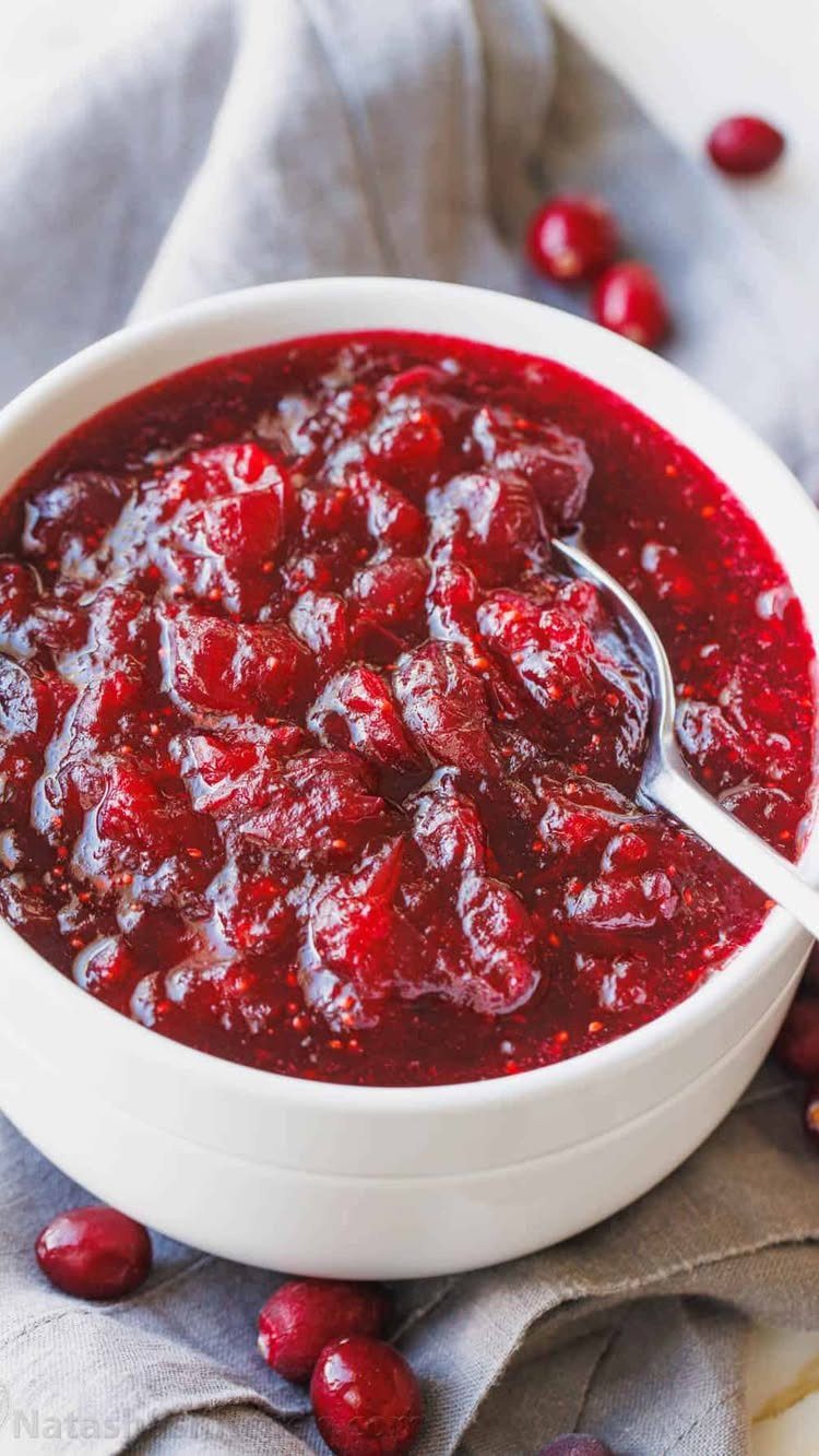 Chunky red cranberry sauce in a white bowl with a silver spoon.