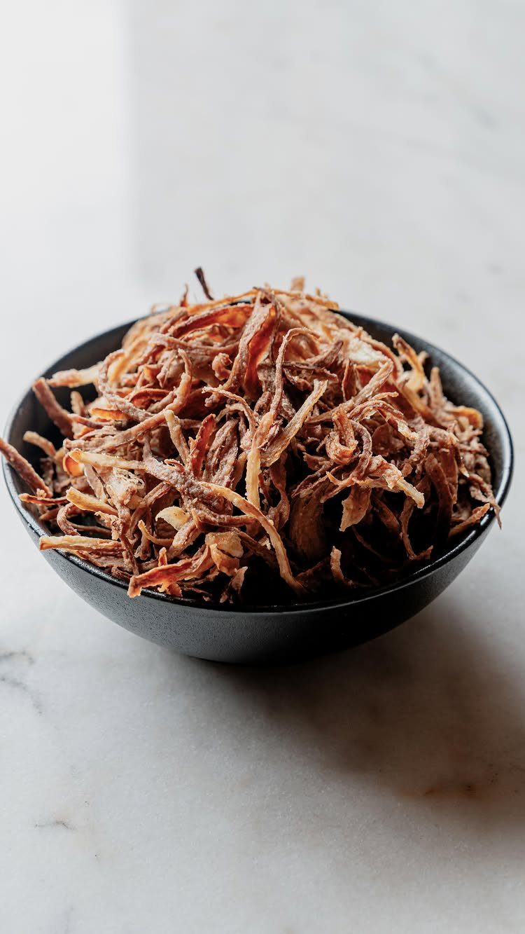 Crispy fried onion strings piled high in a matte black bowl on marble.