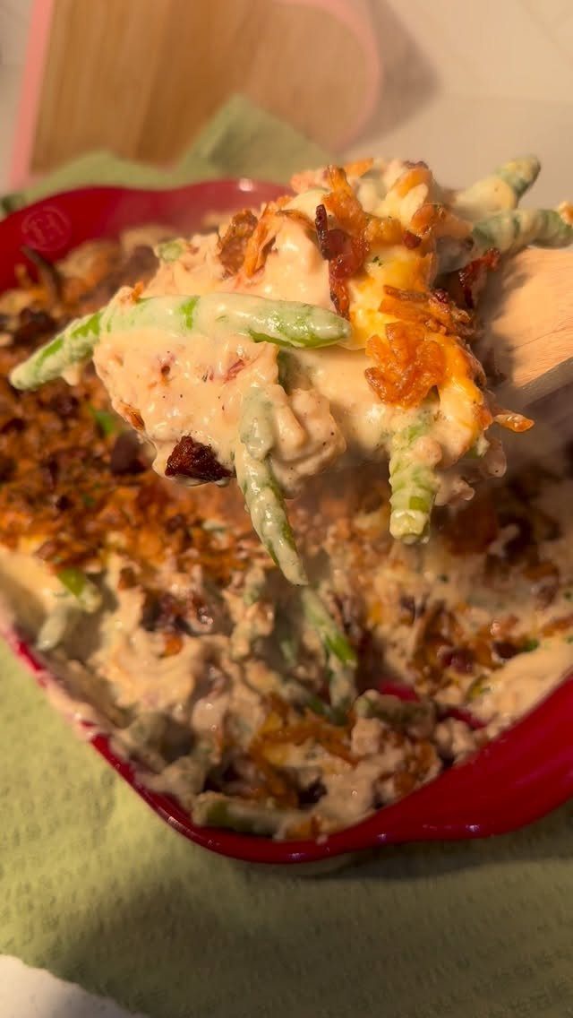 Green bean casserole with creamy sauce and fried onions in a red dish.
