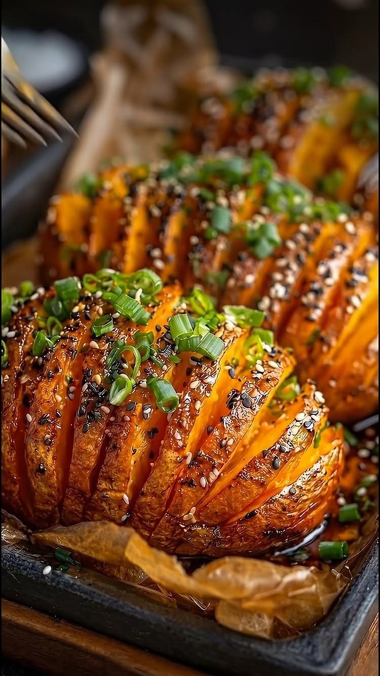 Roasted sliced potatoes topped with sesame seeds and chopped green onions in a tray