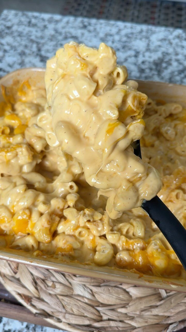 Creamy macaroni and cheese being scooped from a baking dish in a basket.