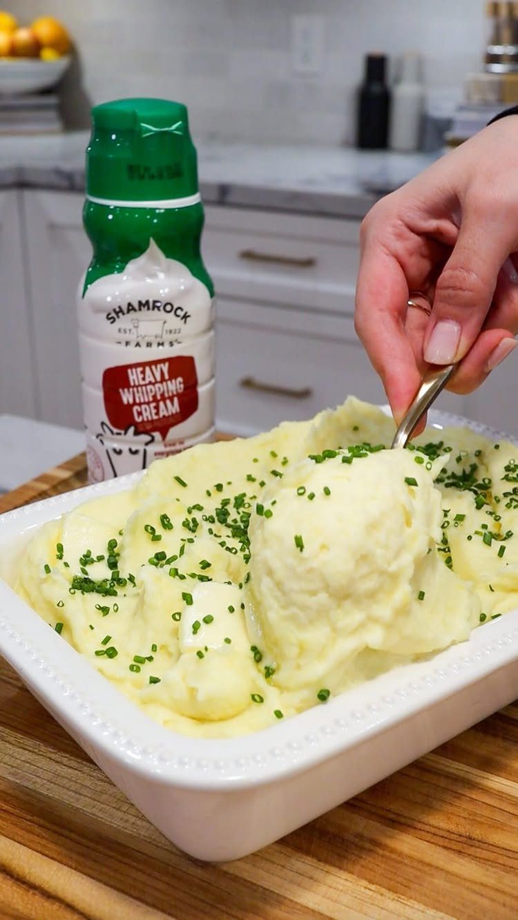 Mashed potatoes with chives in a white dish being scooped by a spoon.