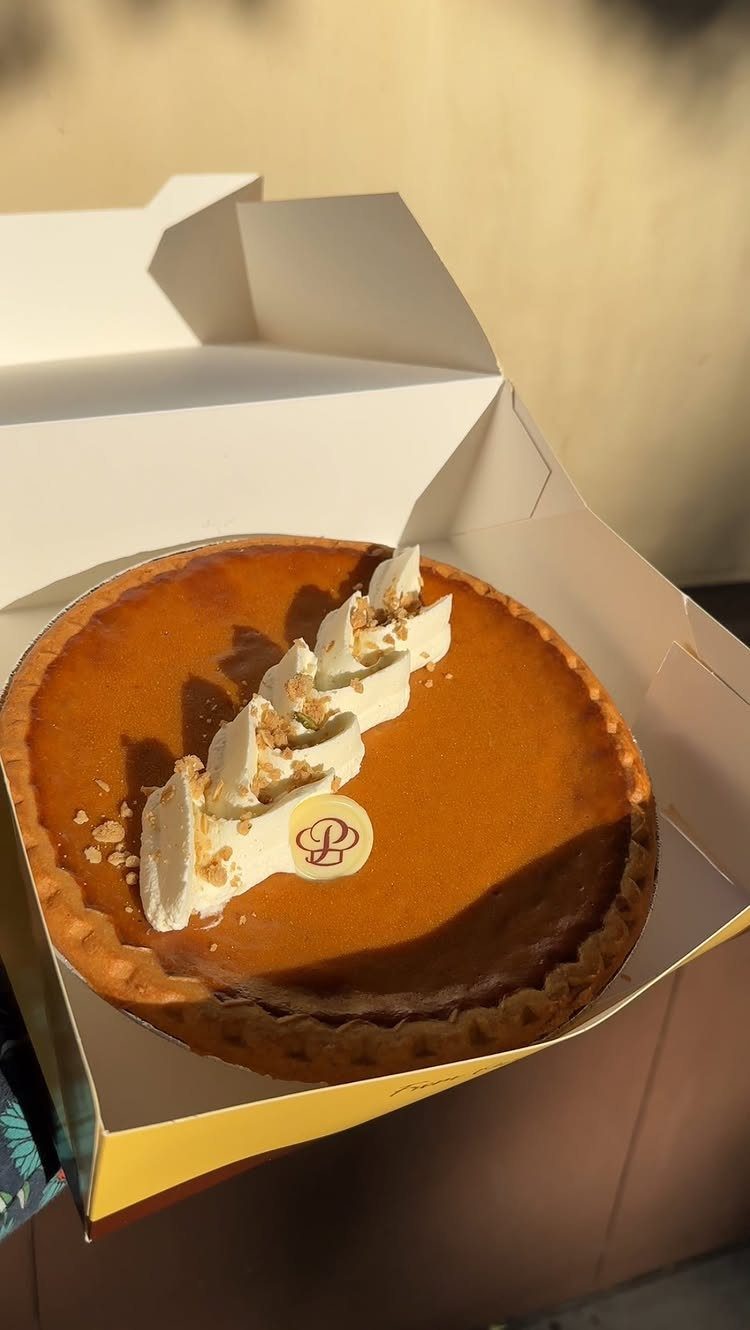 Pumpkin pie with whipped cream and nuts in a white bakery box.