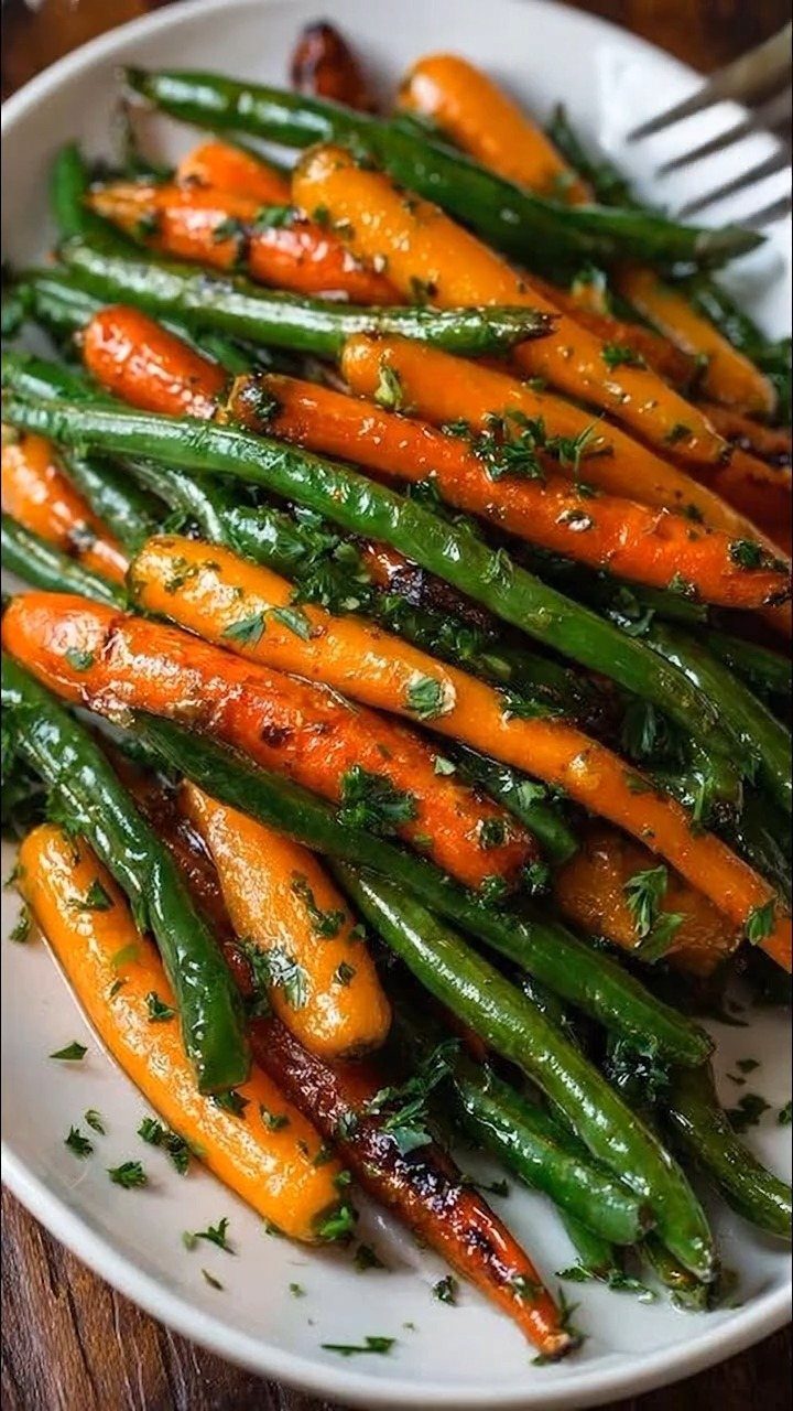 Roasted carrots and green beans garnished with fresh parsley on a white plate.