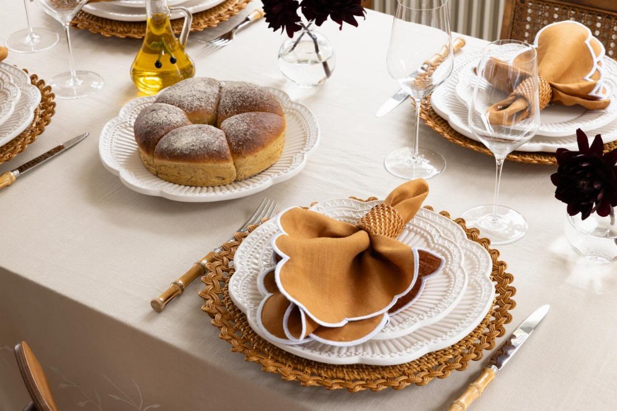 Beige tablecloth with woven jute placemats, white plates, and mustard-yellow napkins.