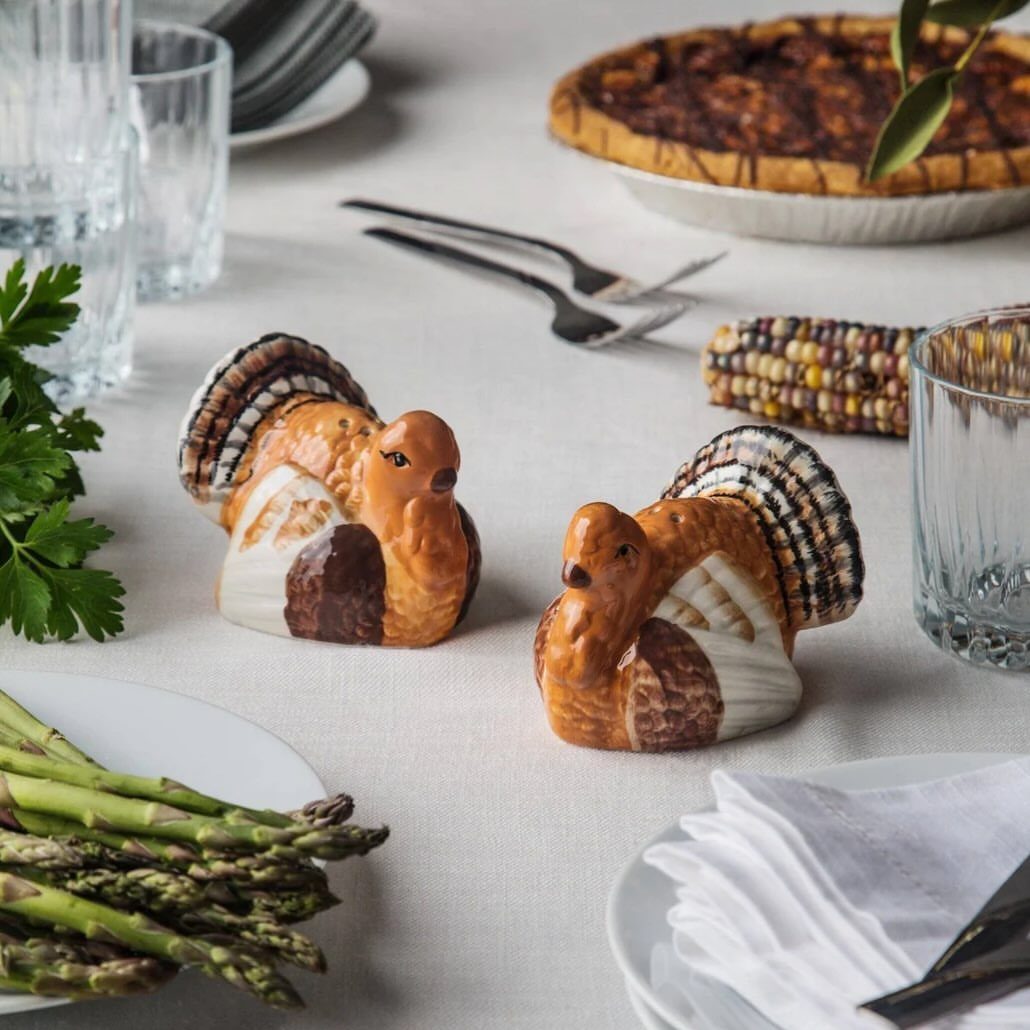 Turkey-shaped salt and pepper shakers on a white Thanksgiving dining table with food.