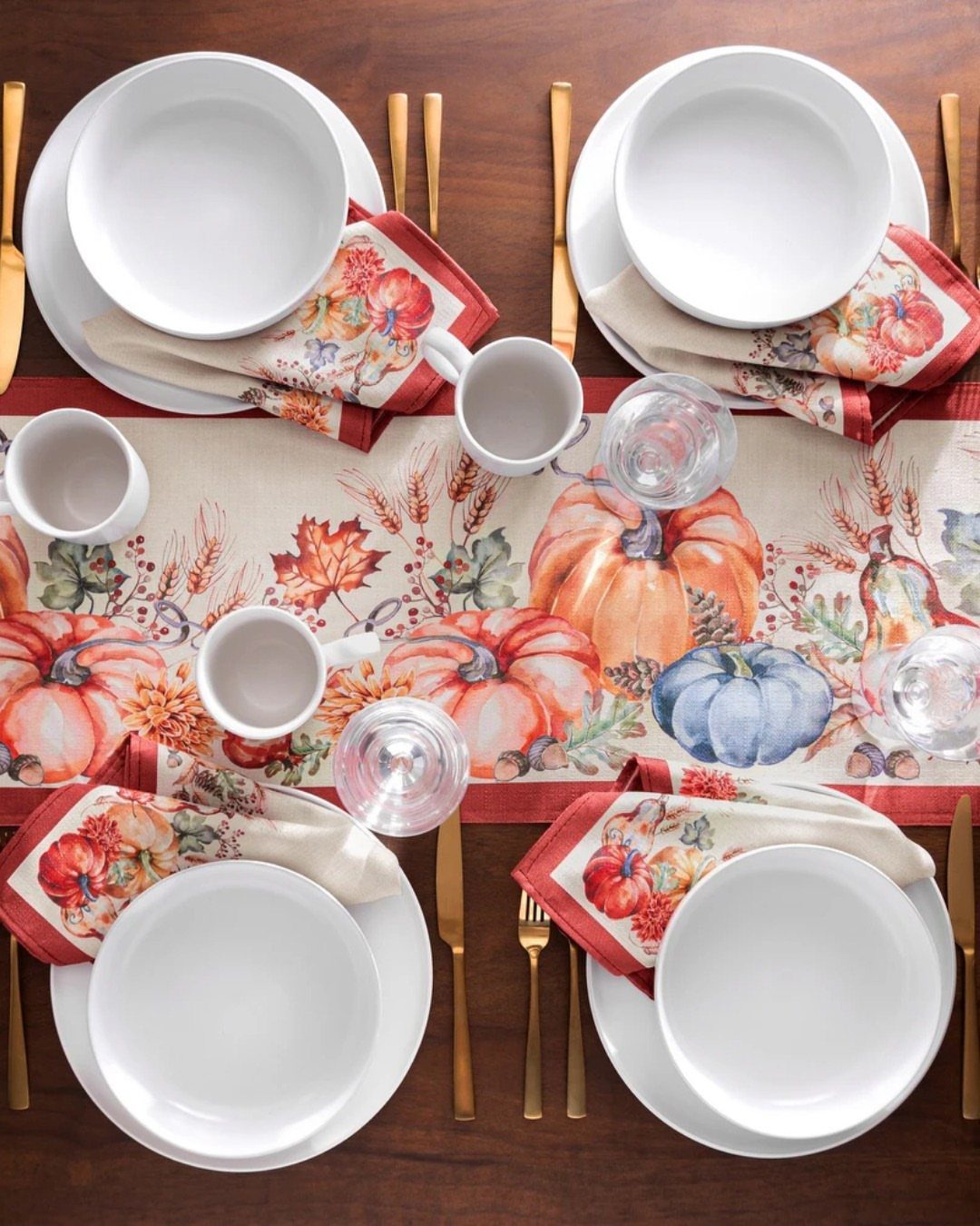 Autumnal table setting with a pumpkin print runner, white plates, and gold cutlery.