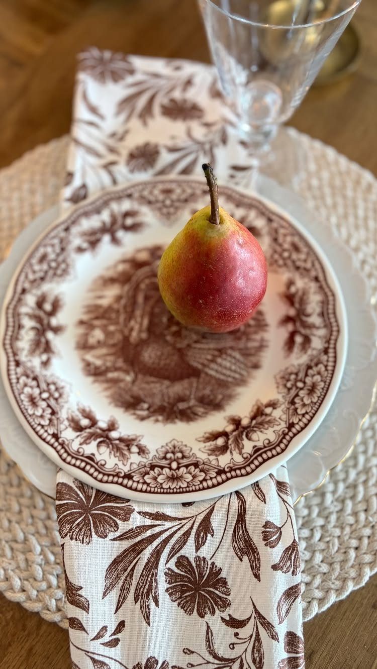 Vintage brown and white patterned plate with a red pear on a woven placemat.