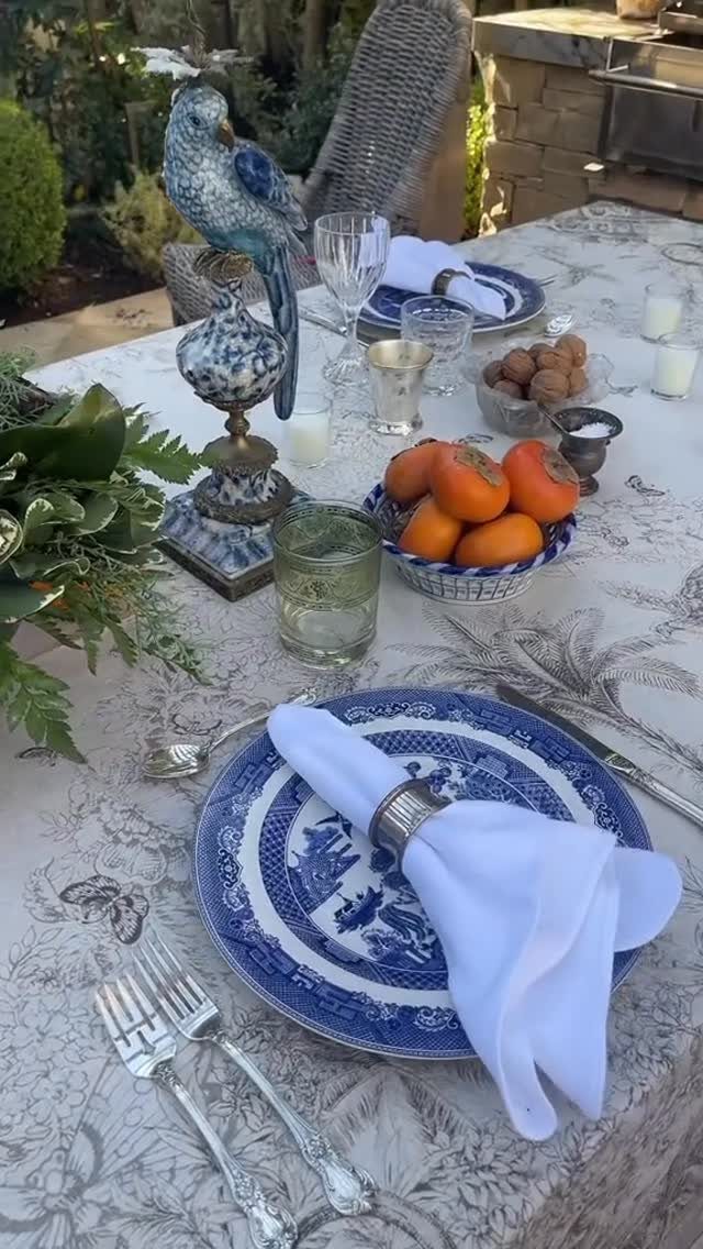 Blue and white ceramic plates on a patterned tablecloth with persimmons and greenery.