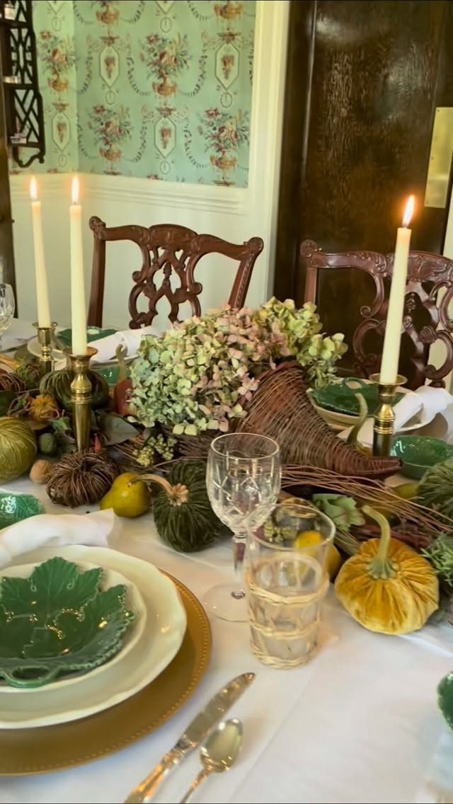 Woven cornucopia centerpiece with green flowers and pumpkins on a set dinner table.