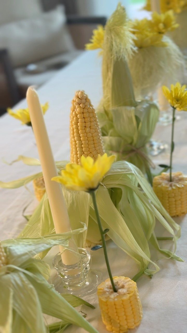 Corn cobs and yellow flowers decorating a white thanksgiving dinner table setting