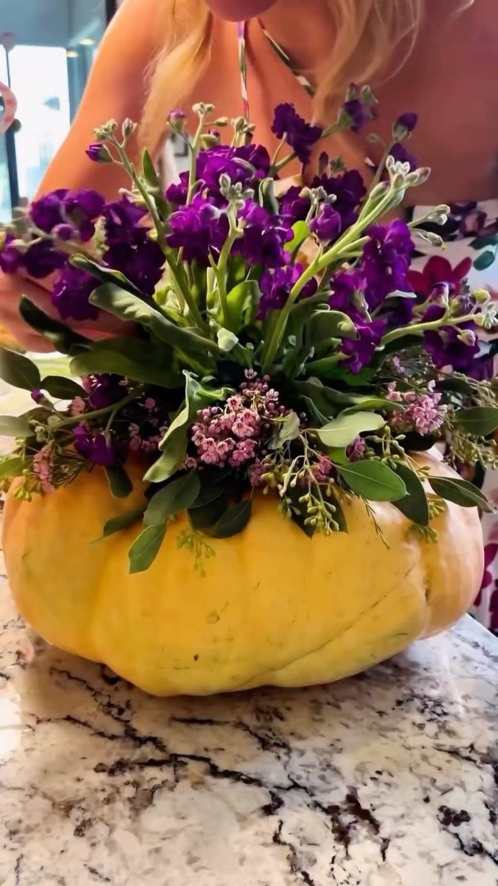 Yellow pumpkin vase filled with purple flowers on a marble countertop