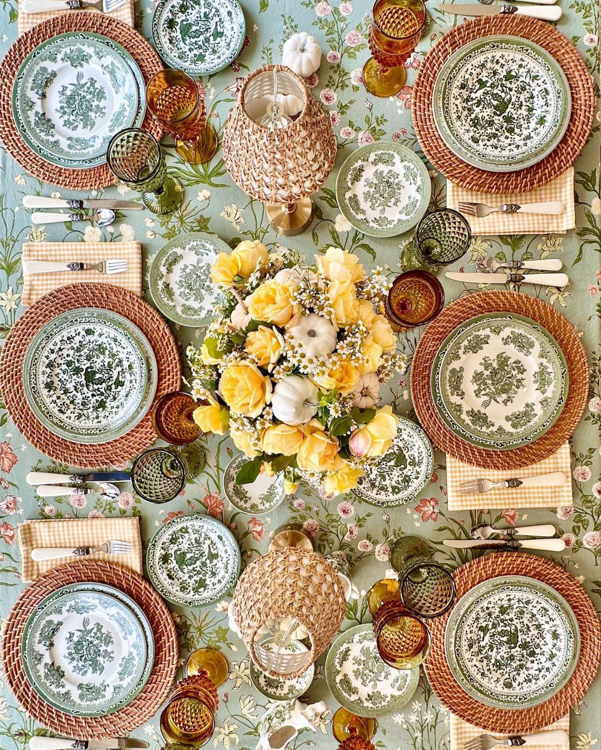 Woven jute placemats and patterned green ceramic plates on a floral tablecloth.