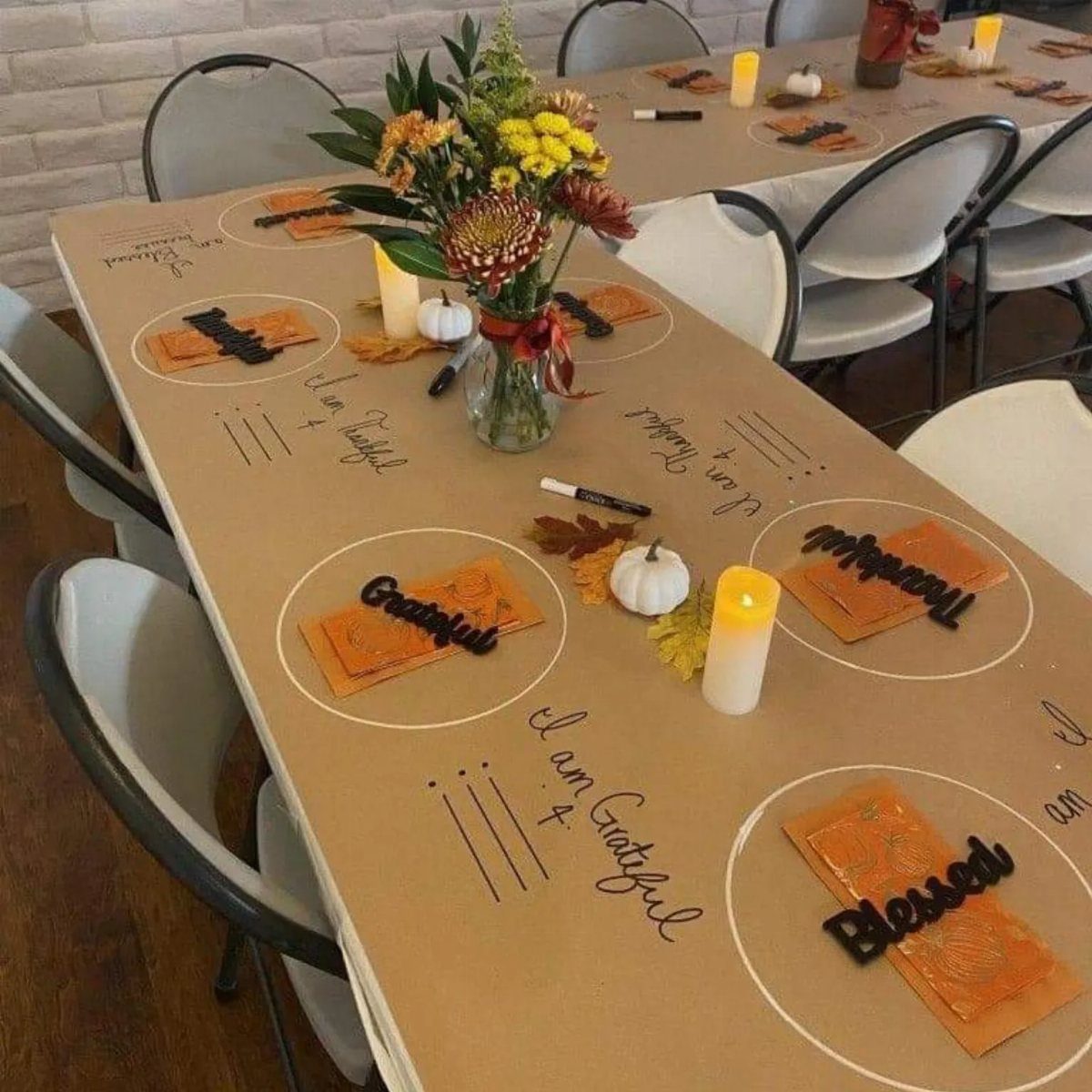 Brown kraft paper table setting with orange napkins, white candles, and floral centerpiece.