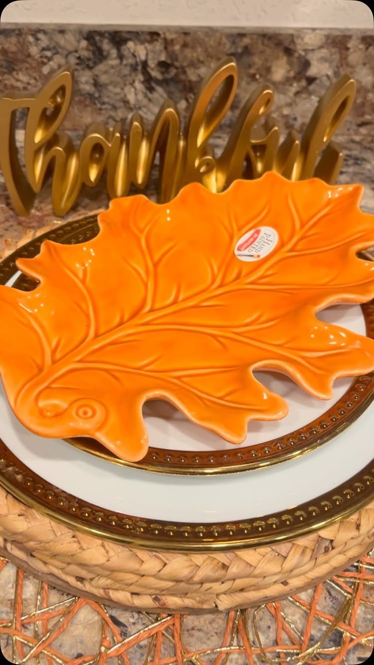 Orange leaf-shaped plate on a gold-rimmed white plate and woven charger
