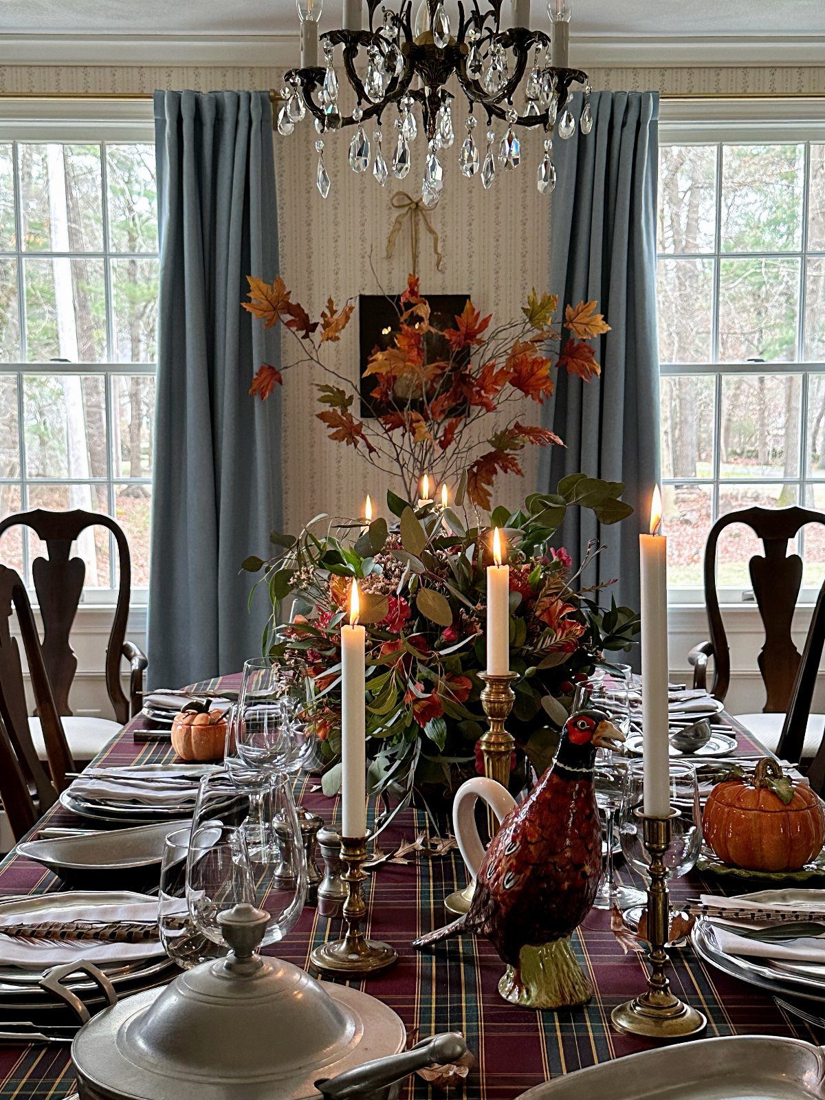 Lavish dining table with autumn floral centerpiece, white candles, and plaid tablecloth.